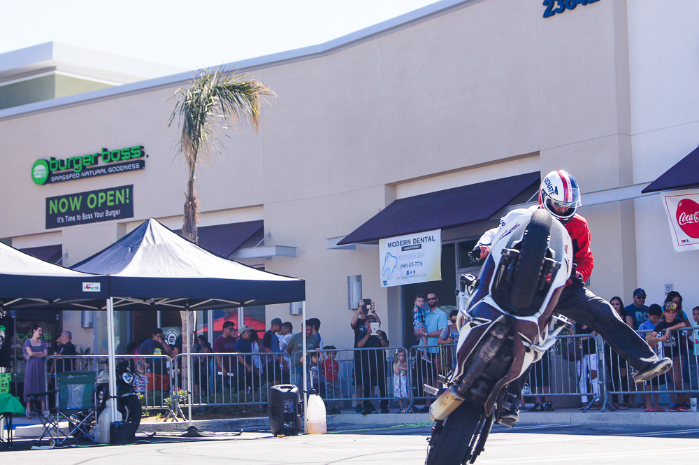 Stunt rider performing a wheelie in the parking lot at the Burger Boss Lake Forest grand opening